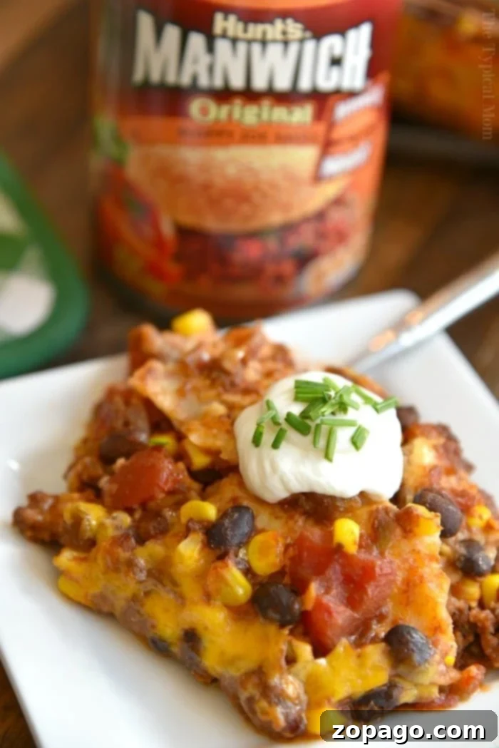 The best enchilada lasagna casserole for family dinner. A plate of cheesy enchilada lasagna loaded with beans, corn, sour cream, and chives sits invitingly. A Manwich can in the background hints at the bold flavors within.