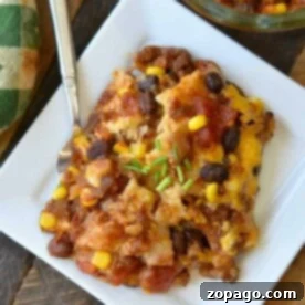 A square plate with a serving of cheesy taco casserole, reminiscent of an enchilada lasagna, topped with chives, sits next to a dish and a green napkin.