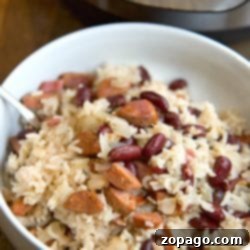 Easy Instant Pot Red Beans and Rice 3 A bowl of rice with kidney beans and sausage, served with a spoon. The Instant Pot red beans and rice dish adds a delightful touch, prominently featured in the background.