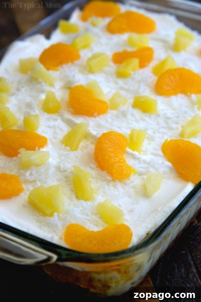 Easy Tropical Poke Cake with Orange and Pineapple Tropical poke cake recipe showing a fully assembled cake with pineapple, orange slices, and coconut flakes.