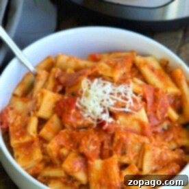 A bowl of rigatoni pasta with a tangy tomato sauce and a generous sprinkle of grated cheese sits invitingly in front of an Instant Pot, bringing to mind the delightful flavors of pizza in every bite.