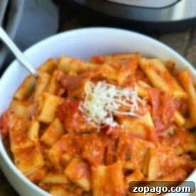 A bowl of rigatoni pasta with a tangy tomato sauce and a generous sprinkle of grated cheese sits invitingly in front of an Instant Pot, bringing to mind the delightful flavors of pizza in every bite.