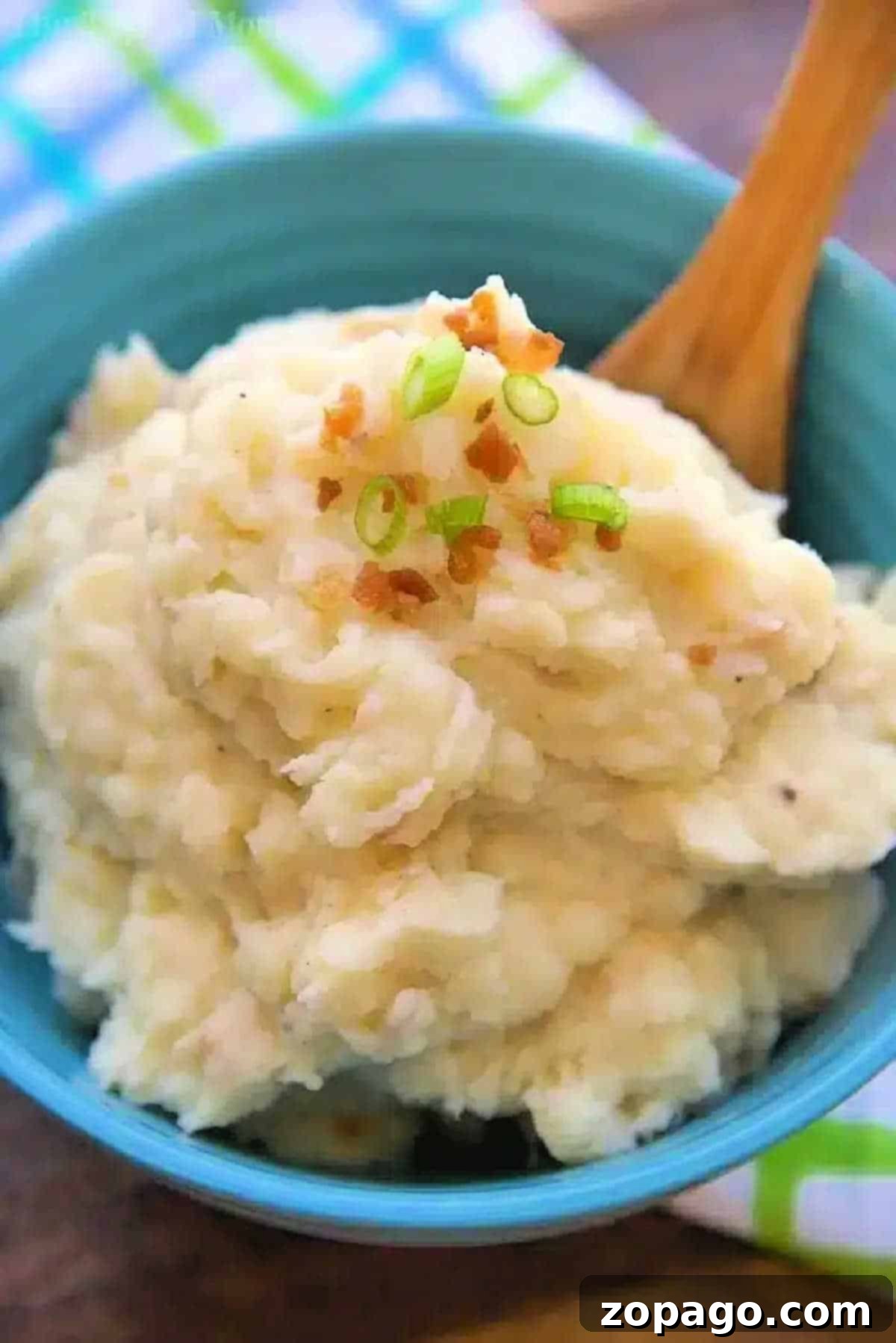 Pressure cooker mashed potatoes in your Instant Pot, Crockpot Express or Ninja Foodi. The easiest way to create this classic buttery side dish for Thanksgiving or year round. A bowl of creamy pressure cooker mashed potatoes topped with chopped green onions and bacon bits, with a wooden spoon in it.