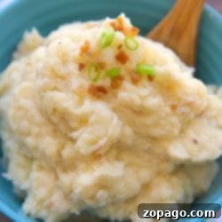 A bowl of pressure cooker mashed potatoes topped with chopped green onions and bacon bits, accompanied by a wooden spoon.