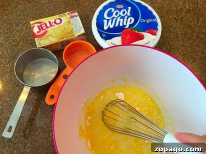 Easy Pudding Frosting for Mug Cakes A bowl of yellow pudding mixture being whisked, surrounded by instant lemon pudding mix, thawed Cool Whip, and a measuring cup, ready to become a delicious mug cake frosting.