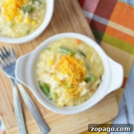 A bowl of creamy pressure cooker chicken and rice soup topped with shredded cheese sits next to two forks on a wooden board.