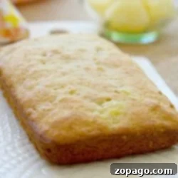 Freshly baked pineapple bread loaf on a white plate, reminiscent of delicious banana pineapple muffins, with a bowl of pineapple chunks in the background.