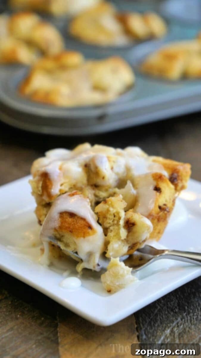 A close-up of a frosted cinnamon roll muffin on a white plate with a fork, surrounded by golden-brown apple pie monkey bread muffins in a muffin tin.