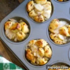 A muffin tin with baked apple pie monkey bread muffins, some golden brown and filled with diced apples.