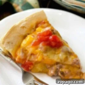 A slice of Copycat Taco Bell Mexican Pizza on a white plate with a fork, reminiscent of a Taco Bell Mexican Pizza, topped with melted cheese and diced tomatoes.