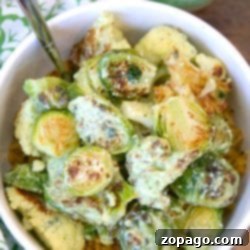 Bowl of roasted Brussels sprouts and cauliflower coated in green sauce, served over hearty grains with a fork—perfect for fans of Roasted Brussel Sprouts and Cauliflower.