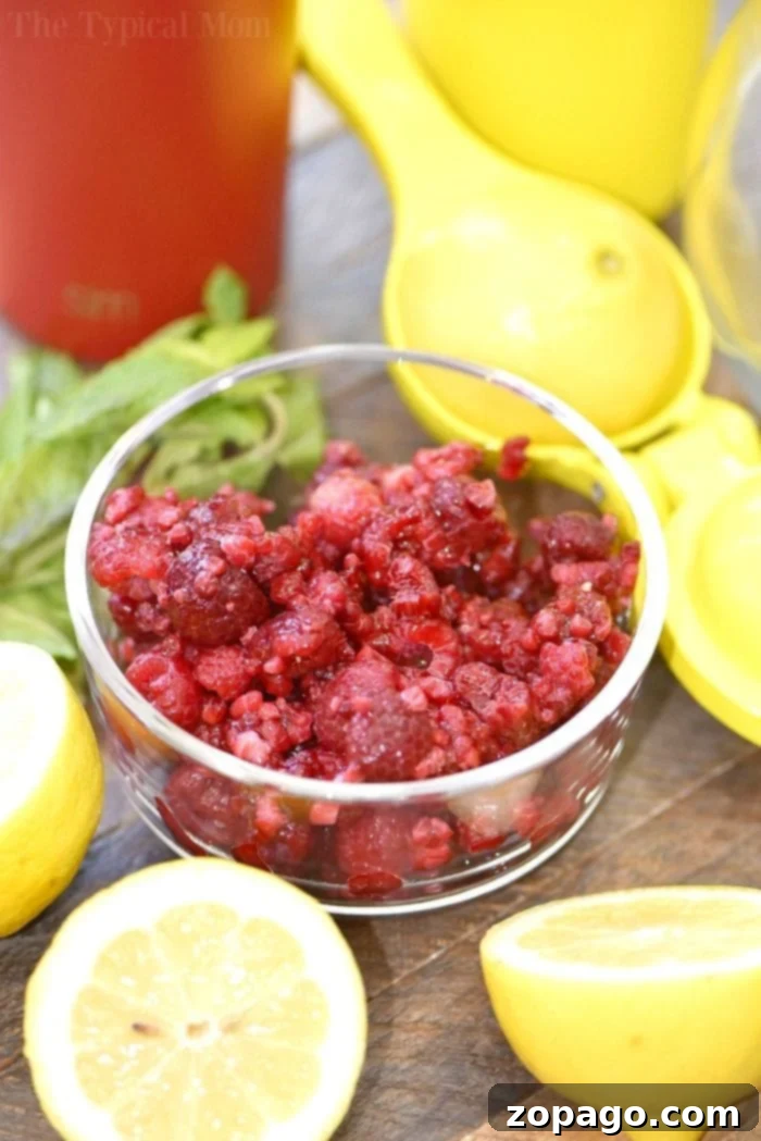 This homemade raspberry lemonade recipe only requires 4 ingredients and is perfect for Summertime! Packed with fresh fruit it's my favorite on the go drink. #homemade #raspberry #lemonade #drink #juice Close-up of vibrant pink homemade raspberry lemonade with ice, fresh raspberries, and mint leaves, ready to be enjoyed.