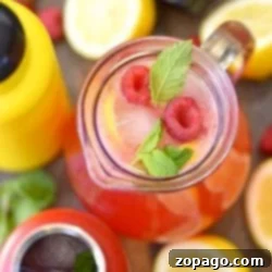 Top view of a pitcher with homemade raspberry lemonade, ice, mint, and lemons surrounded by drink bottles and fresh fruit.