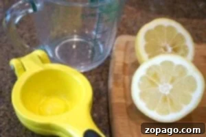 A lemon cut in half, a yellow juicer, and a measuring cup sit on a wooden cutting board, ready to create that perfect fresh squeezed lemonade recipe.