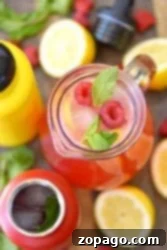 Top view of a pitcher with homemade raspberry lemonade, ice, mint, and lemons surrounded by drink bottles and fresh fruit.