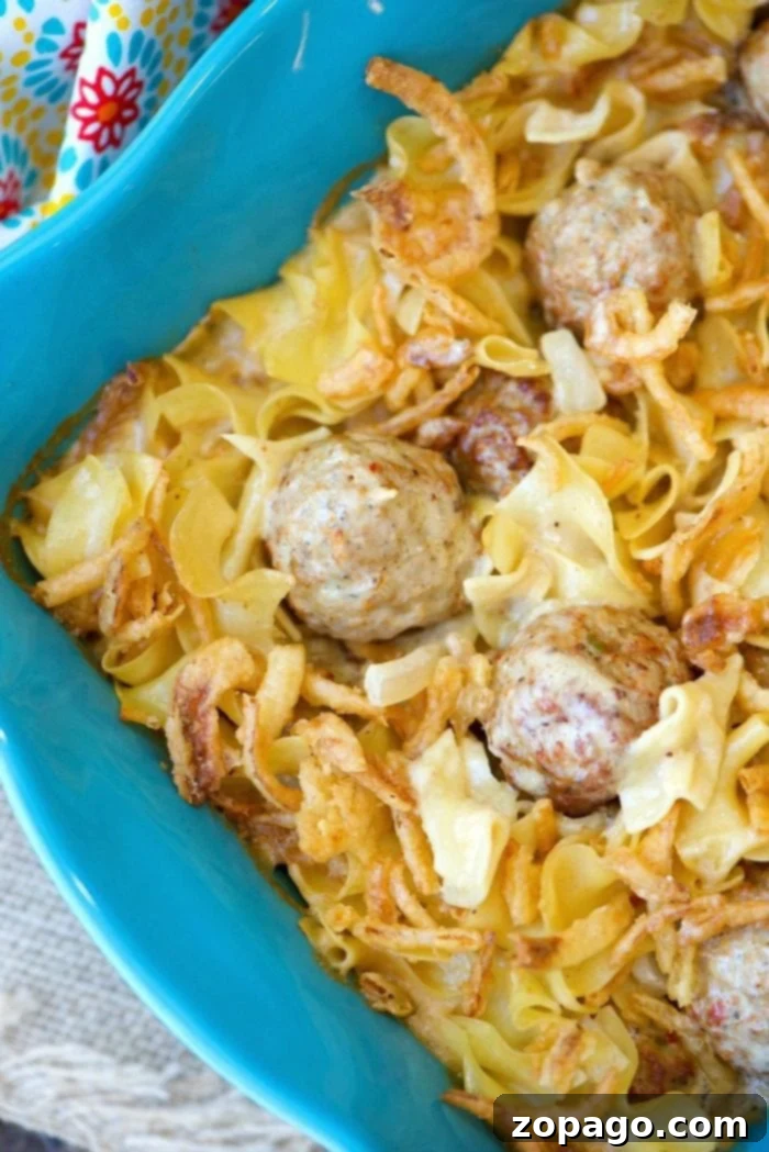 Easy Swedish meatball casserole recipe with pasta, creamy sauce, and crispy onions. A quick and delicious comfort food meal for any night. A top-down view of an easy Swedish meatball casserole with pasta in a blue baking dish, garnished with golden crispy onions.