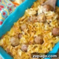 A blue baking dish brimming with pasta and an easy Swedish meatball casserole, topped with a creamy sauce. Baked to perfection, it rests beside a wooden spoon. A colorful patterned cloth adds a touch of warmth in the background.