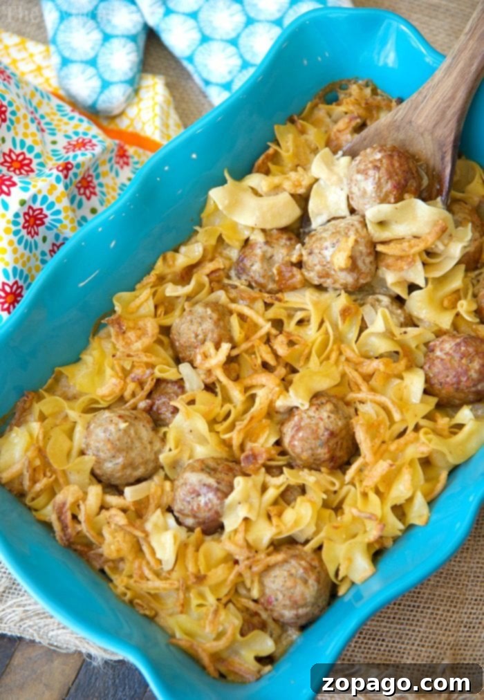 A large, inviting blue baking dish filled with creamy Swedish meatball casserole and egg noodles, garnished with herbs and a wooden spoon nearby, set on a rustic wooden surface.