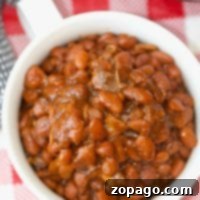 A bowl of no soak Instant Pot baked beans rests on a red and white checkered tablecloth.