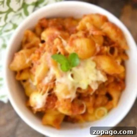 A bowl of crockpot lasagna, garnished with fresh green herbs, is presented on a wooden table beside a patterned cloth, inviting a comforting meal.