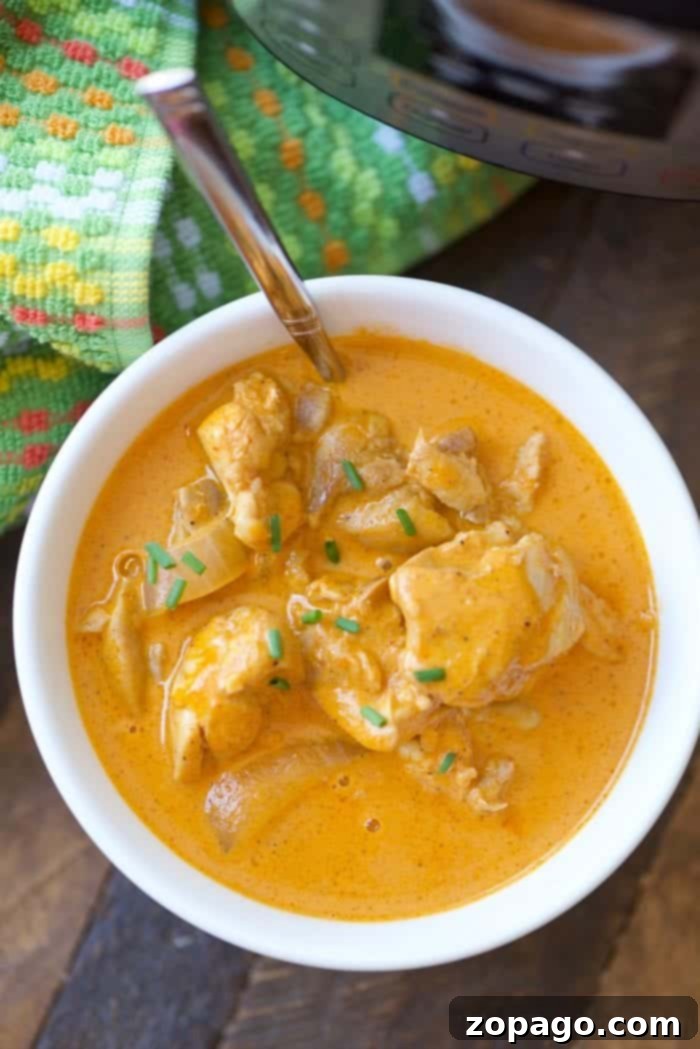 Instant Pot chicken recipes you can make for dinner! We love this fancy pressure cooker and chicken can be cooked in no time at all. We have made frozen chicken in the Instant Pot too! Check out this long list of really healthy meals your family will love. #instantpotrecipes #pressurecooker #chicken #healthy #recipes #instantpot #easy #dinners #thetypicalmom A bowl of creamy chicken curry, one of those easy instant pot chicken recipes, garnished with herbs. A spoon and a colorful cloth sit nearby, ready for a delightful meal experience.