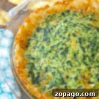 A tater tot spinach quiche sits invitingly in a glass pie dish on a wooden table, surrounded by a cheerful yellow cloth and a vibrant blue napkin.