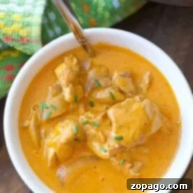 A bowl of easy Instant Pot butter chicken, featuring tender chicken chunks and green herbs on top, with a spoon nestled inside.