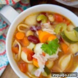 A bowl of easy instant pot minestrone soup with shell pasta, beans, and a parsley garnish sits invitingly on a wooden table.