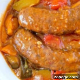 One-Pot Slow Cooker Sausage and Vegetables 4 Crockpot sausage simmered in a tomato-based sauce with vibrant red and yellow bell peppers, served in a white bowl.