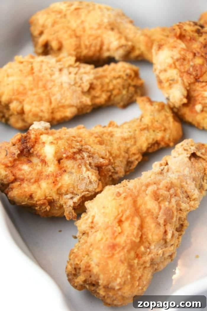 Crispy, juicy homemade copycat fried chicken ready to be served. Enjoy four pieces of crispy fried chicken on a white plate, crafted with our special copycat Kentucky Fried Chicken recipe.