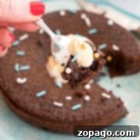 A hand with red nails holds a fork poised over a blue plate, ready to indulge in an Instant Pot chocolate cake adorned with luscious frosting.