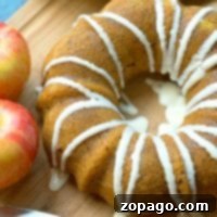 A bundt cake with white icing drizzled on top sits on a wooden cutting board.