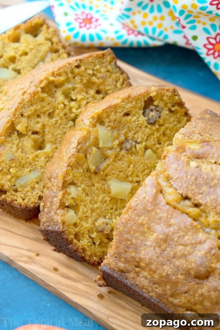 Easy pumpkin apple bread recipe that's a perfect breakfast or dessert for Fall! Moist pumpkin bread packed with diced apples and nuts is our favorite treat. Slices of easy pumpkin apple bread with walnuts rest on a wooden board, accompanied by a floral cloth in the background.