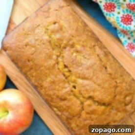 A perfectly baked loaf of pumpkin apple bread on a wooden board, surrounded by fresh apples.