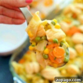 A spoonful of easy chicken pot pie casserole with peas, corn, and carrots is held above a baking dish.