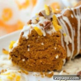 Slice of easy gingerbread pumpkin bundt cake with white icing drizzle and nuts on top, resting on a white plate.