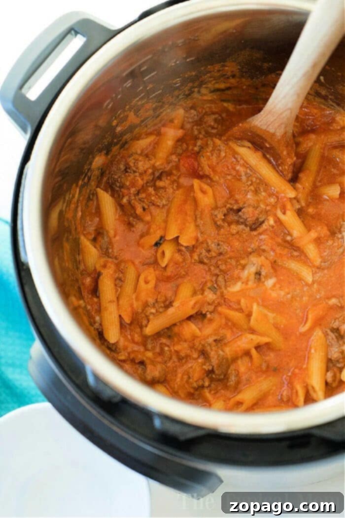 One Pot Pressure Cooker Lasagna 4 Pasta with meat sauce being stirred with a wooden spoon inside an Instant Pot for a delicious pressure cooker lasagna casserole.