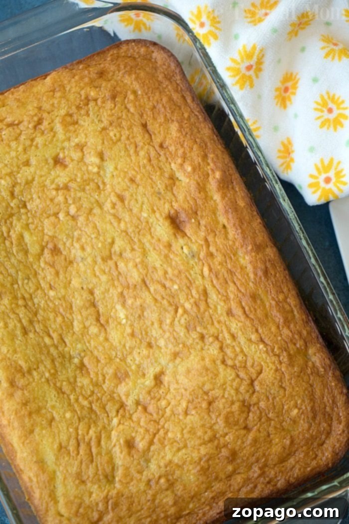 The best banana pudding cake you'll ever make! Loaded with ripe bananas and a touch of cinnamon this easy cake turns out moist and delicious every time. #bananacake #cake #pudding #puddingcake Golden baked banana pudding cake in a glass dish next to a floral yellow and white napkin, reminiscent of a cozy cake mix afternoon.