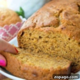 Spiced Pumpkin Banana Loaf 4 A person slices into a loaf of moist, golden-brown pumpkin banana bread on a white plate.