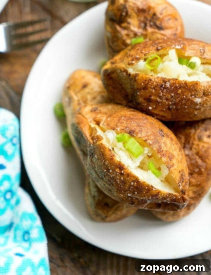 Ultimate Ninja Foodi Baked Potatoes 7 Ninja Foodi baked potatoes split open and topped with chopped green onions on a white plate, ready to eat.
