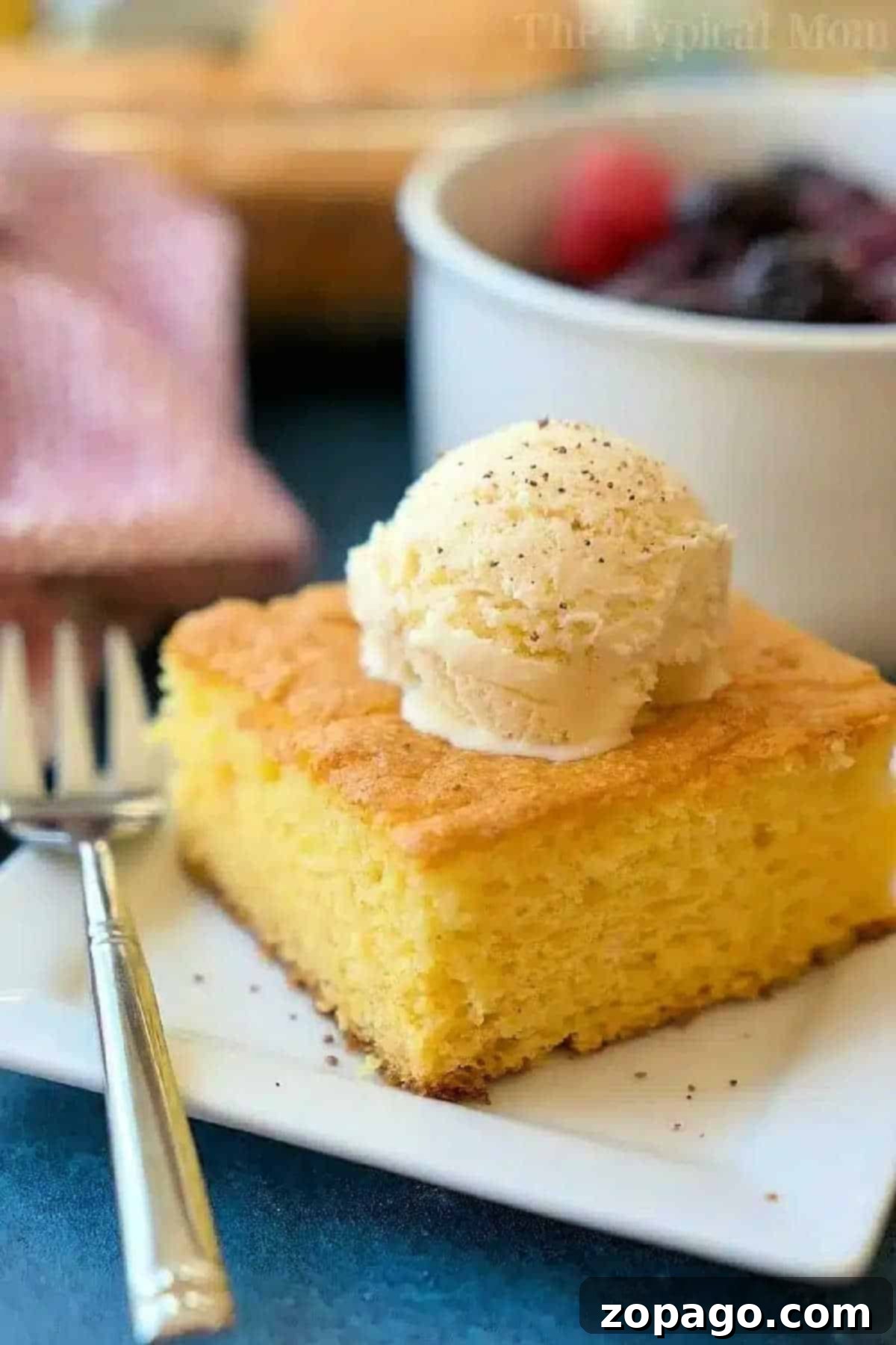 Holiday Eggnog Pudding Cake 2 A perfectly sliced piece of moist egg nog pudding cake, generously topped with a scoop of creamy vanilla ice cream, presented on a pristine white plate alongside a fork, ready to be enjoyed as a festive holiday dessert.