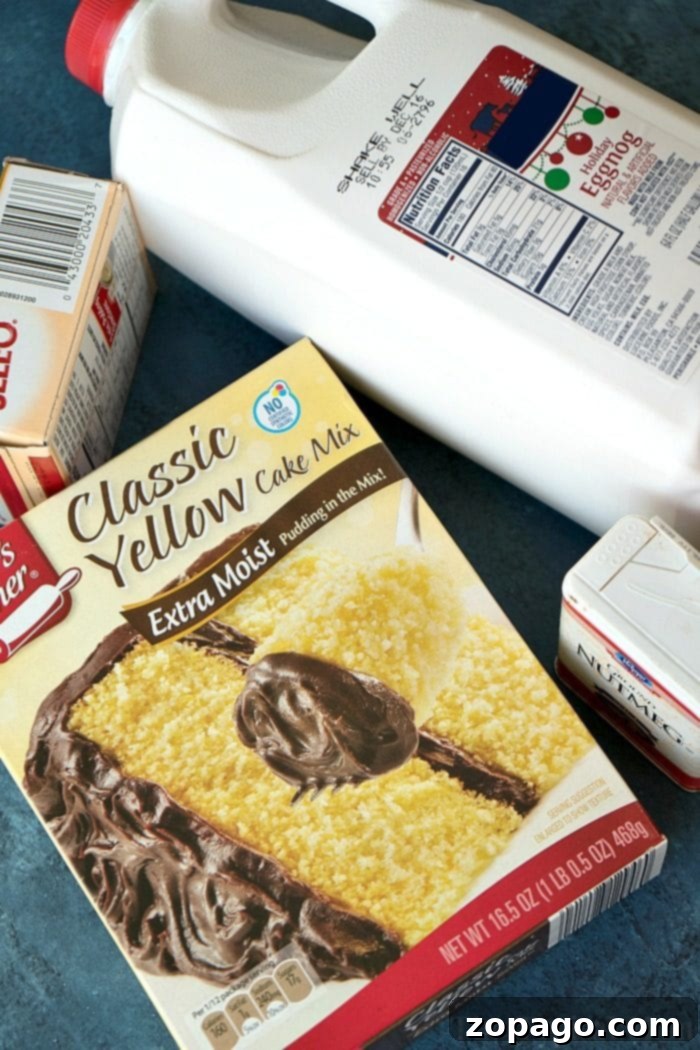 Holiday Eggnog Pudding Cake 3 A classic yellow cake mix box, a carton of rich egg nog, two fresh eggs, a bottle of vegetable oil, and a dash of nutmeg laid out on a blue surface, representing the simple ingredients for a delectable egg nog pudding cake.