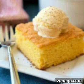 A mouthwatering slice of egg nog pudding cake, elegantly topped with a generous scoop of vanilla ice cream, served on a modern square white plate with a fork.