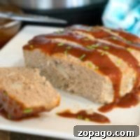 A sliced turkey meatloaf topped with a glossy brown sauce and garnished with chopped green onions sits on a white square plate. The Instant Pot, which made this tender loaf possible, is visible in the blurred background alongside a blue cloth.