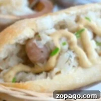 A close-up of an instant pot brat nestled in a bun, topped with mustard, sauerkraut, and chives.