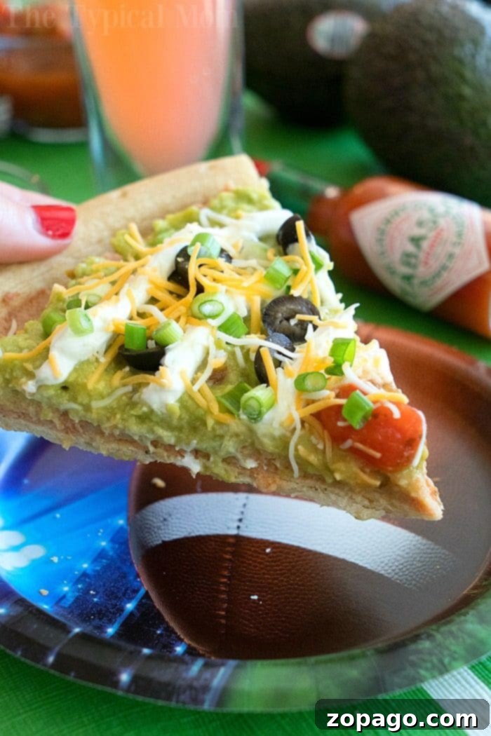 Loaded 7 Layer Pizza Dip 7 A slice of 7 layer dip pizza, ready to be picked up and enjoyed at a Super Bowl party.