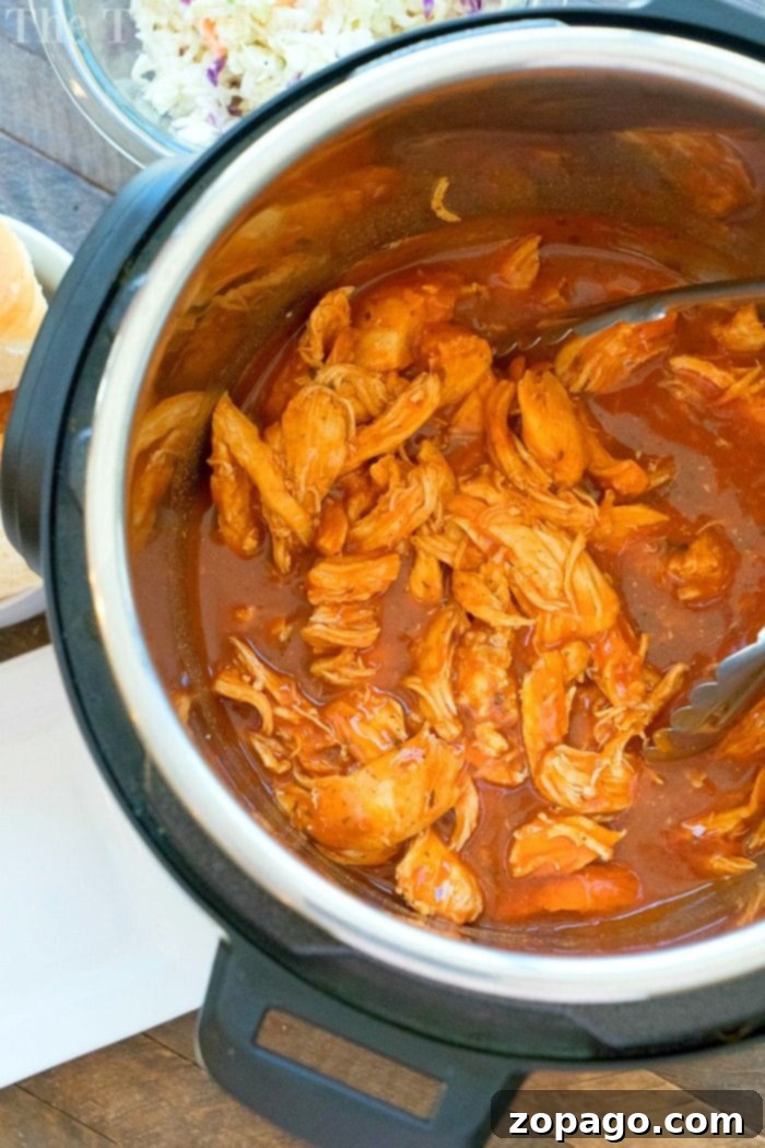 Spicy electric pressure cooker chicken sliders are the perfect appetizer or dinner for your family! Get ready for Super Bowl with your Instant Pot and just 3 ingredients to make the easiest snack that will fly off the table at your party this year. Bring on the heat! #superbowl #appetizer #instantpot #pressurecooker #chicken #instantpotrecipe #thetypicalmom #sliders Close-up of shredded buffalo chicken on a Hawaiian roll with coleslaw