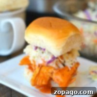 Pulled chicken sliders with coleslaw rest on a square white plate, accompanied by a mug, hinting at their tender perfection from the pressure cooker.