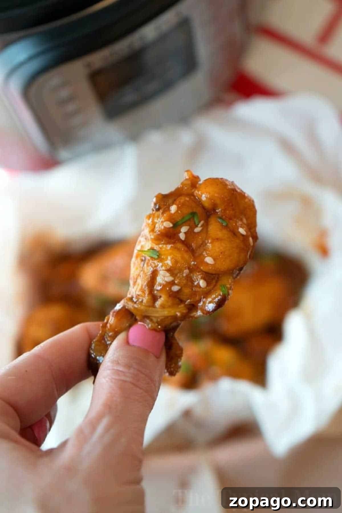 Effortless Pressure Cooker Frozen Chicken Wings 2 A close-up of a hand holding a succulent, saucy barbecue chicken wing, garnished with sesame seeds and fresh herbs, inviting viewers to make their own tender pressure cooker frozen chicken wings at home.