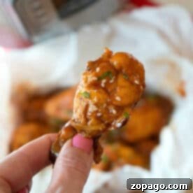A hand holds a saucy chicken wing, topped with sesame seeds and herbs—perfect inspiration for making juicy pressure cooker frozen chicken wings at home.